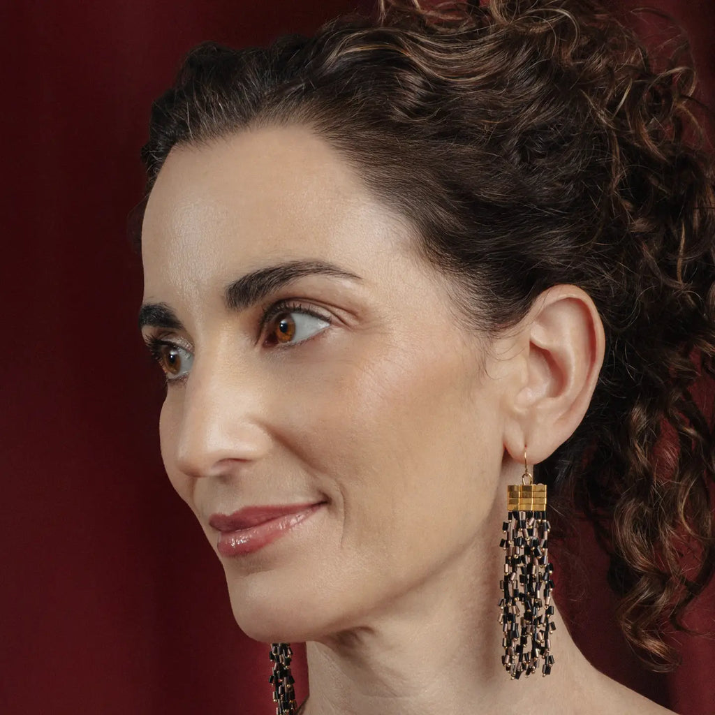Woman wearing beaded gold and black earrings with a red background
