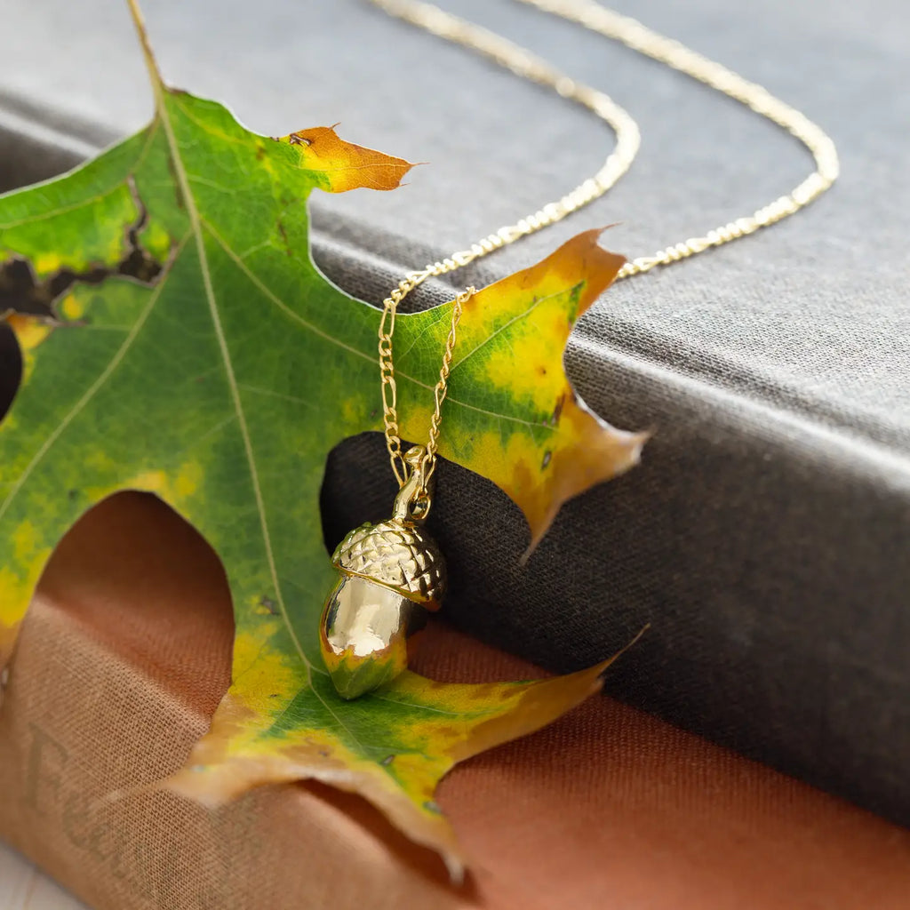 Gold acorn pendant necklace on a green leaf