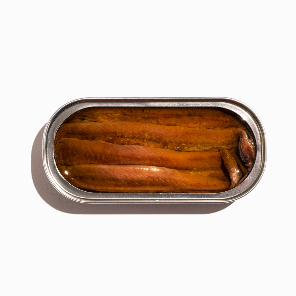 Open tin of canned anchovies on a white background