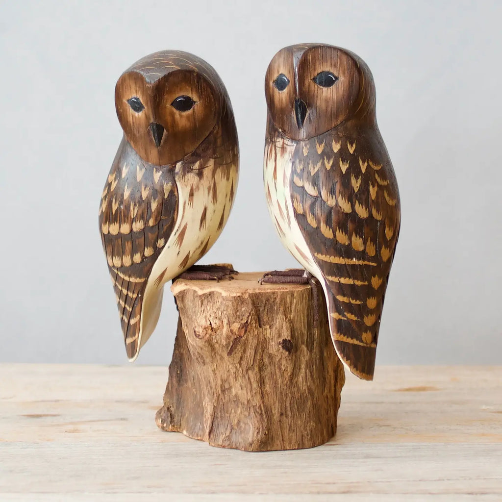 Wooden owl figurines on a wooden stump against a light gray background