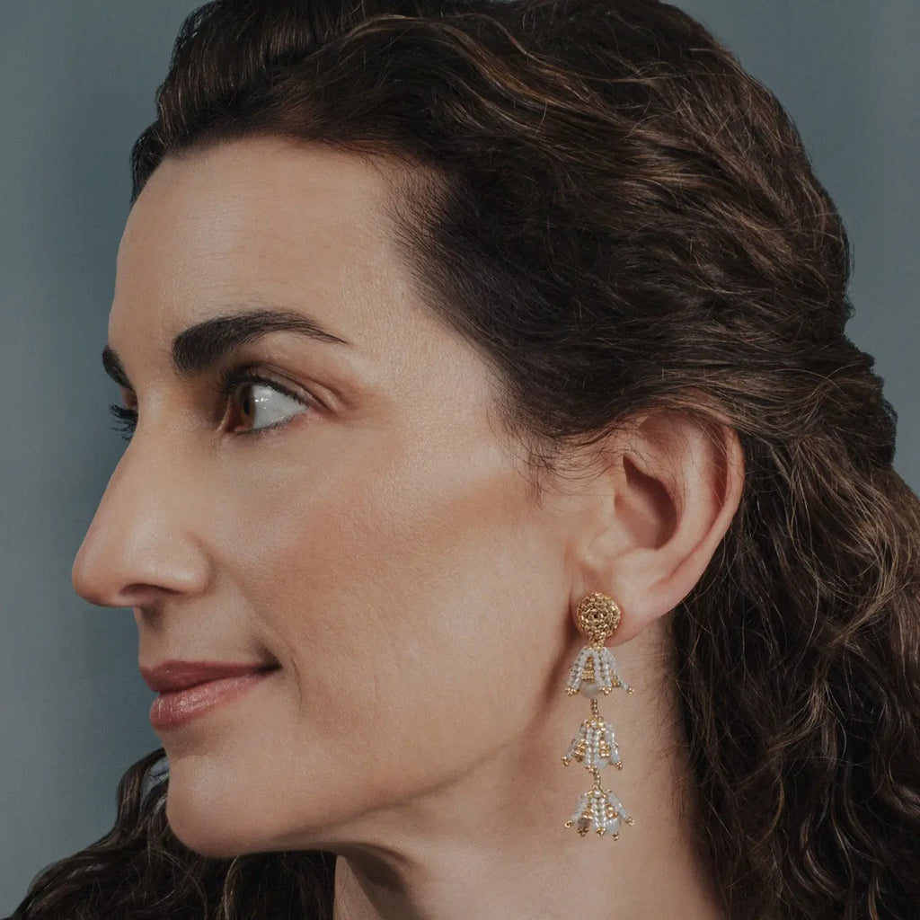 Close-up of a woman wearing gold beaded and pearl earrings with a gray background