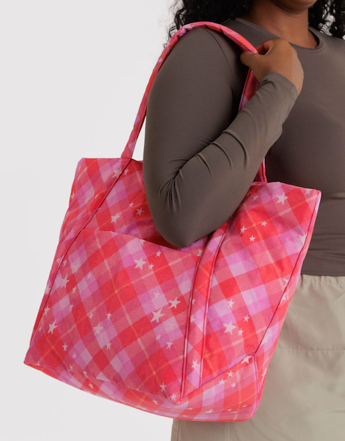 Person holding a pink plaid bag with yellow stars on a plain background