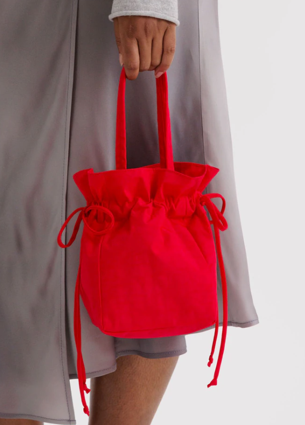 Red drawstring bag held by a person wearing a gray dress.