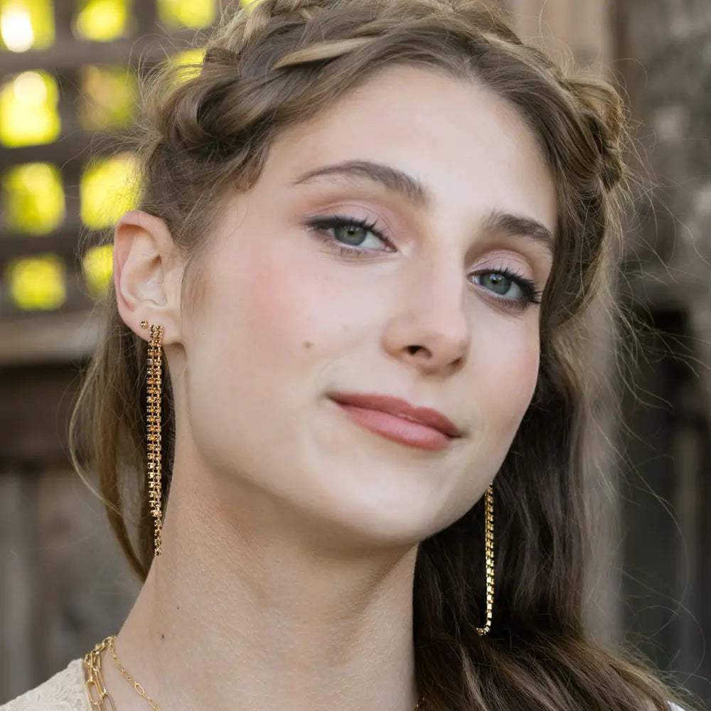 Close-up of a woman wearing gold crystal dangle earrings with a blurred background