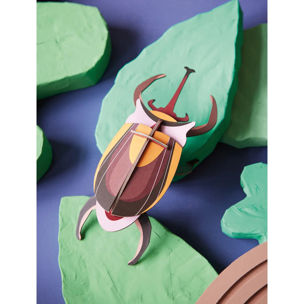 Colorful beetle-shaped object on green leaves with a blue background