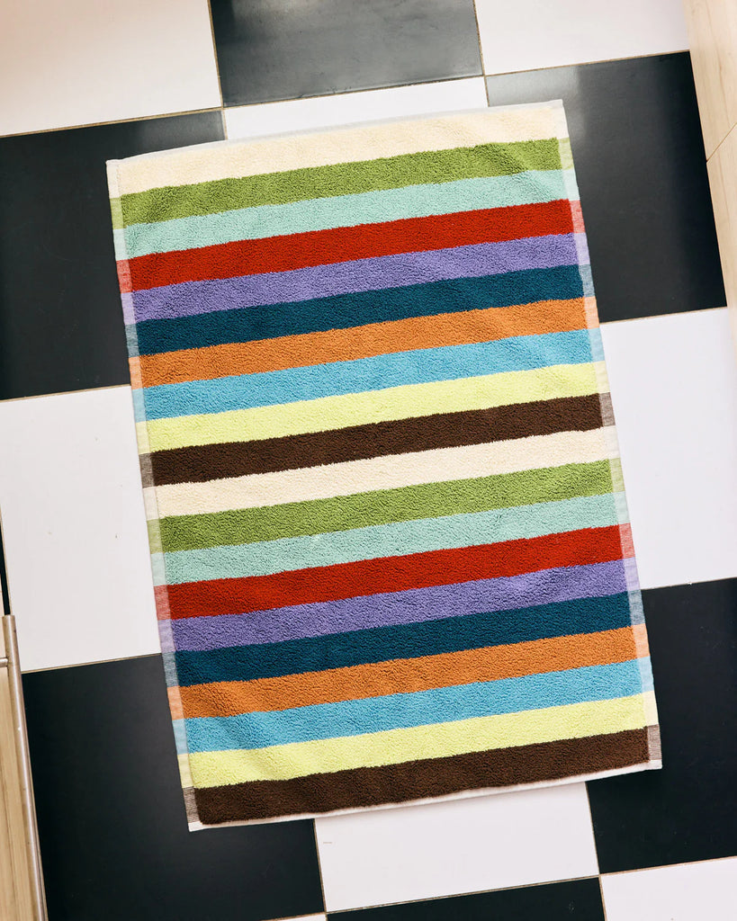 Red, purple, teal, orange, brown, blue and cream multicolored striped terry bath matt on a checkered floor