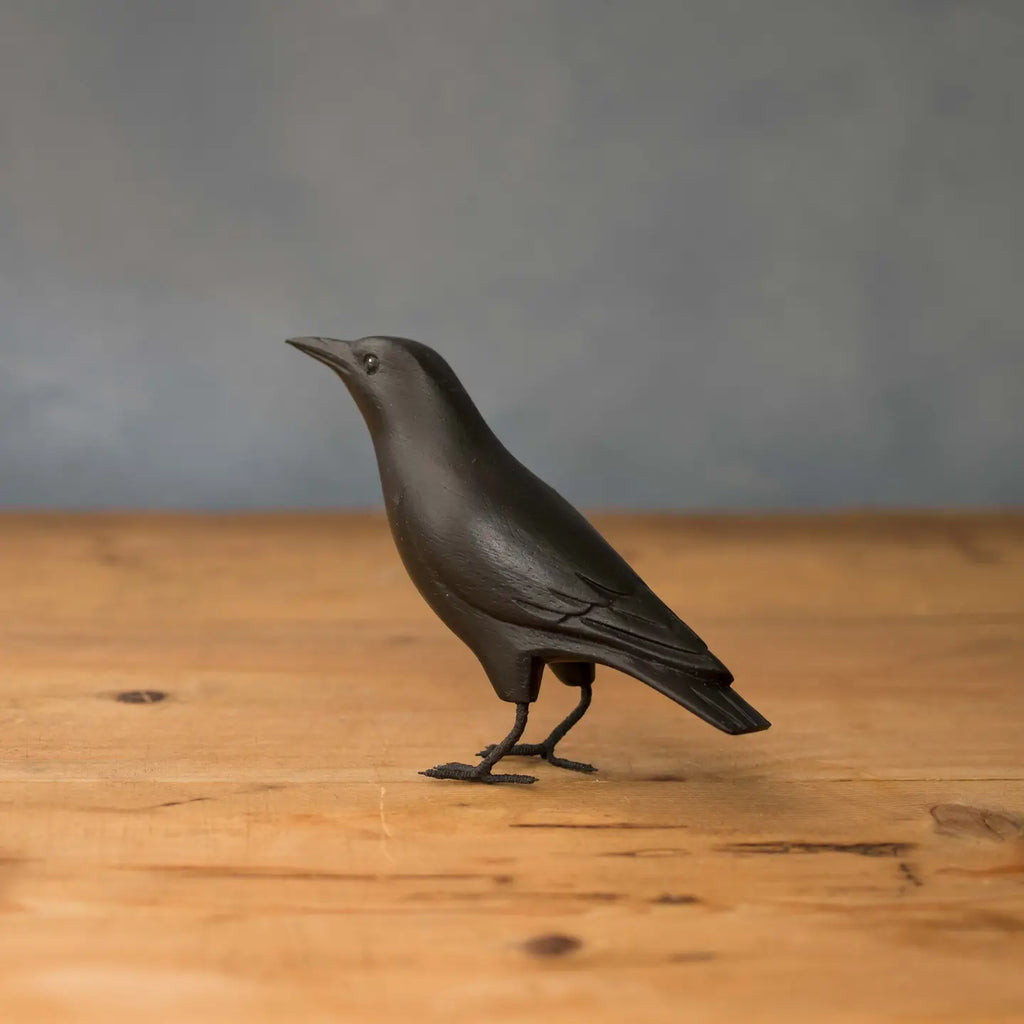 Carved wooden crow bird sculpture on a wooden surface with a gray background