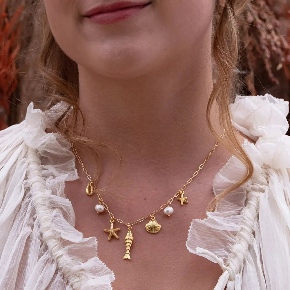 Close-up of a woman wearing a gold necklace with various charms against a blurred background.