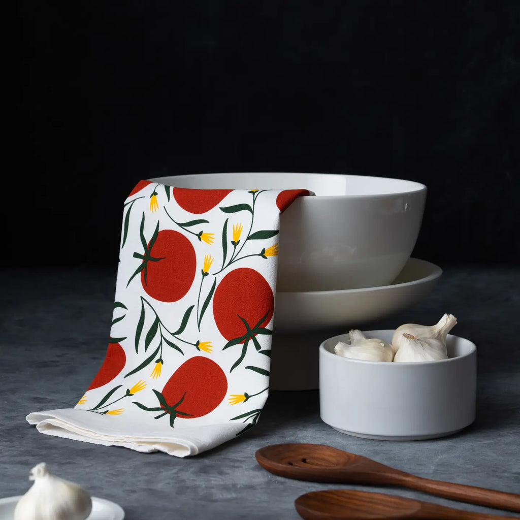 Kitchen towel with tomato pattern draped over a white bowl on a dark surface.