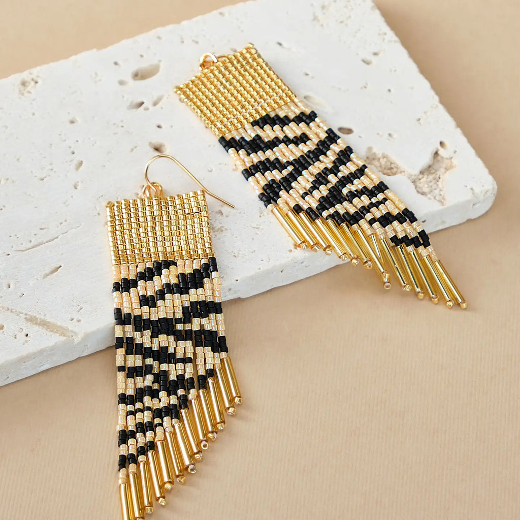 Gold and black beaded earrings on a textured surface