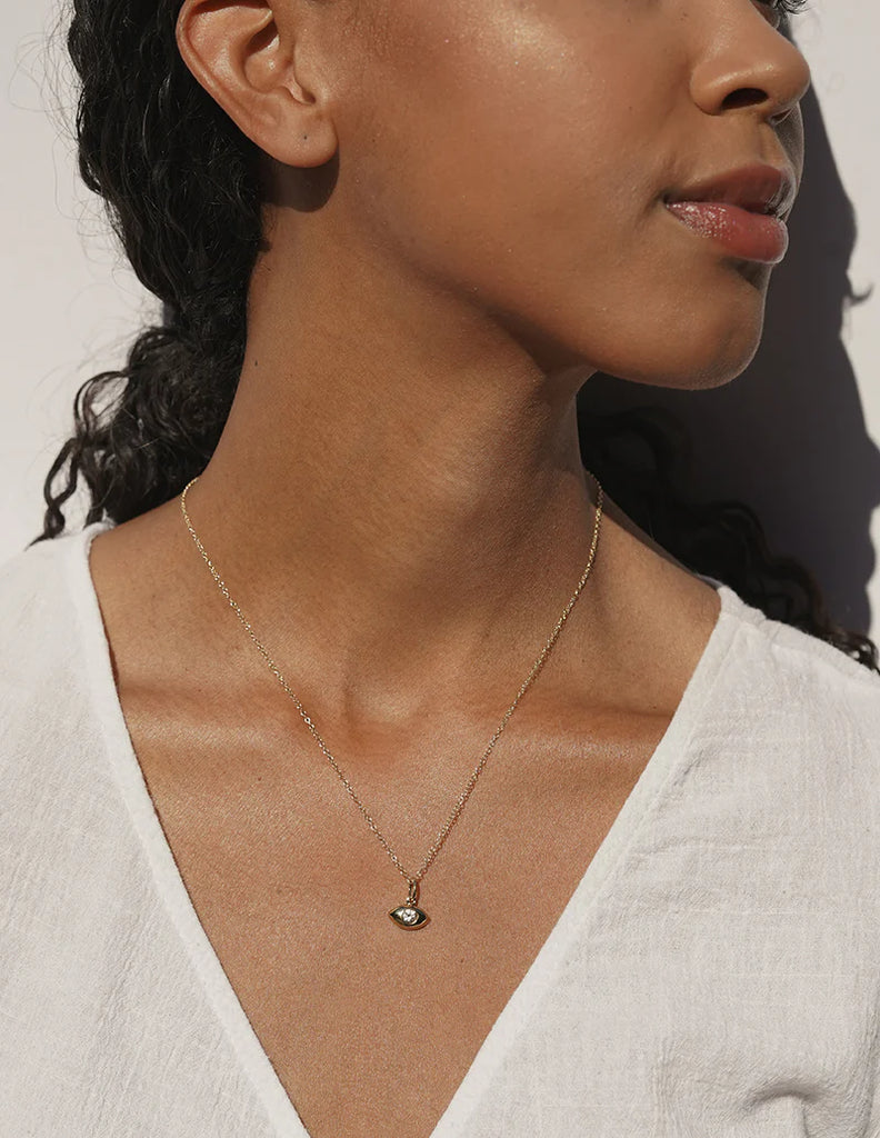 close up of a Black woman wearing a necklace with a gold evil eye on it